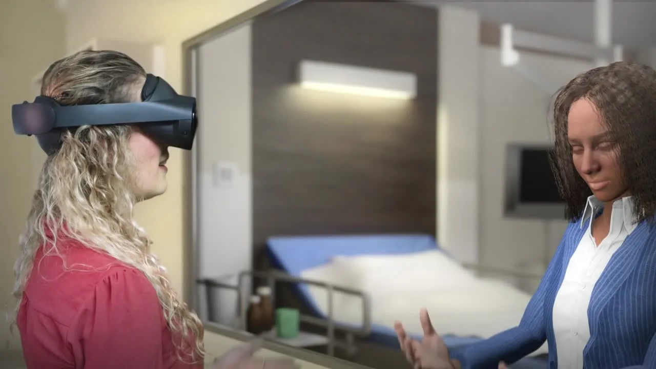 A woman wearing a headset stands face to face with her mirrored reflection in a simulated hospital room, both with their hands raised mid-conversation.