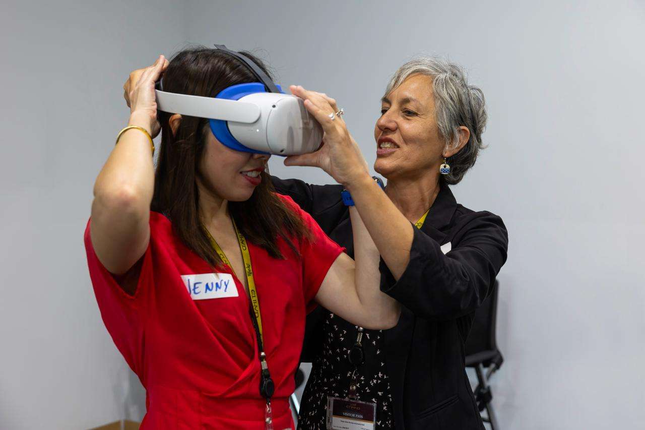 Photo of a facilitator fitting a VR headset onto a participant wearing an Etihad visitor pass, during a PTR-run workshop