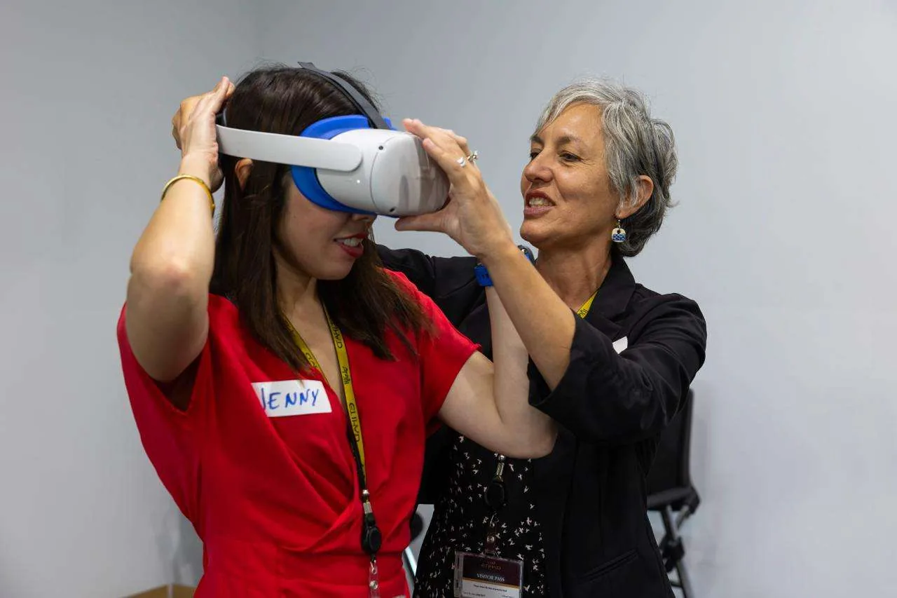 A participant with a handwritten name tag is fitted with a VR headset by another attendee, both wearing Etihad workshop visitor lanyards.