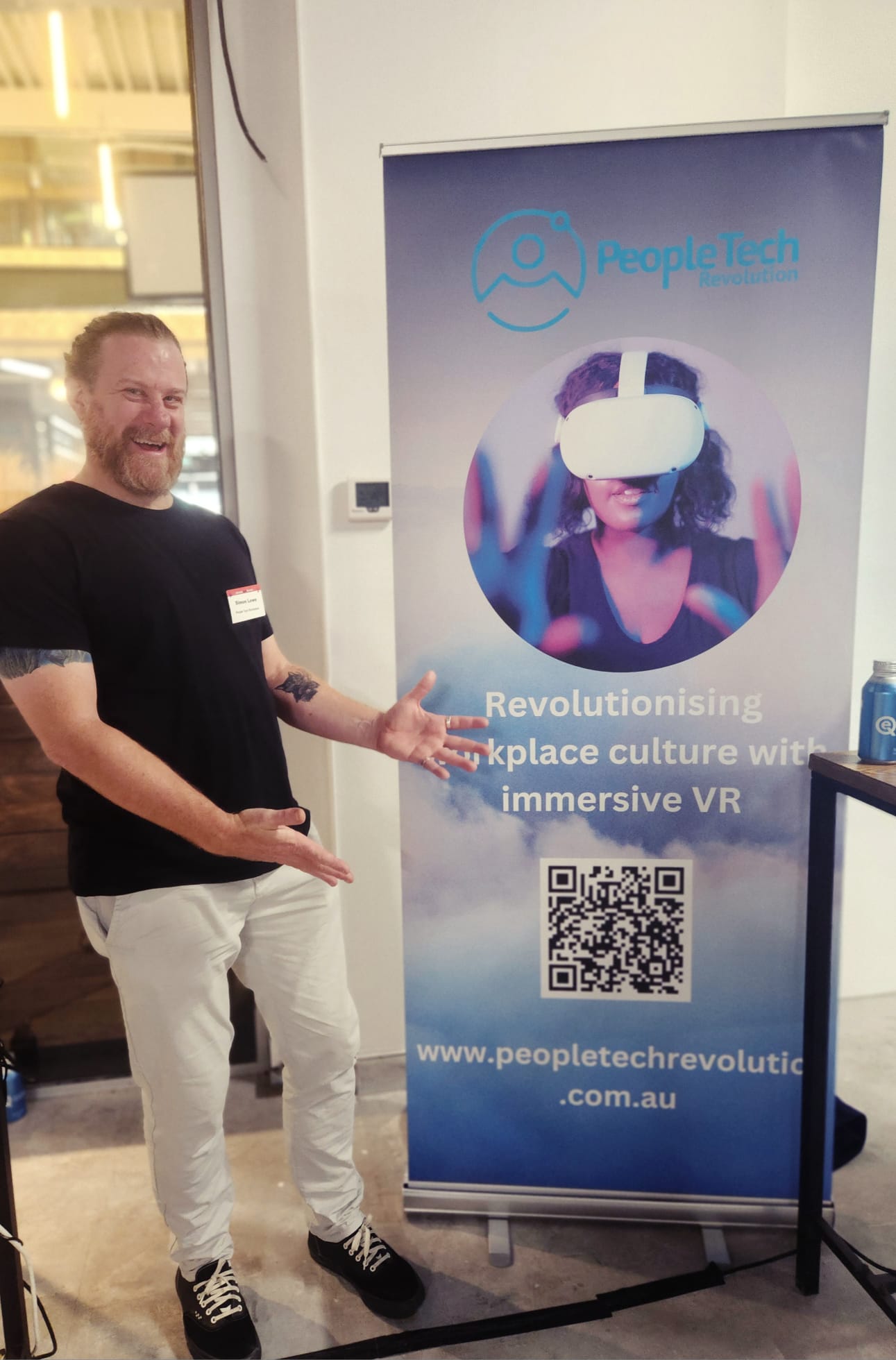 PTR co-founder Simon Lowe gesturing toward a PTR pull-up banner reading 'Revolutionising workplace culture with immersive VR' at a technology council event