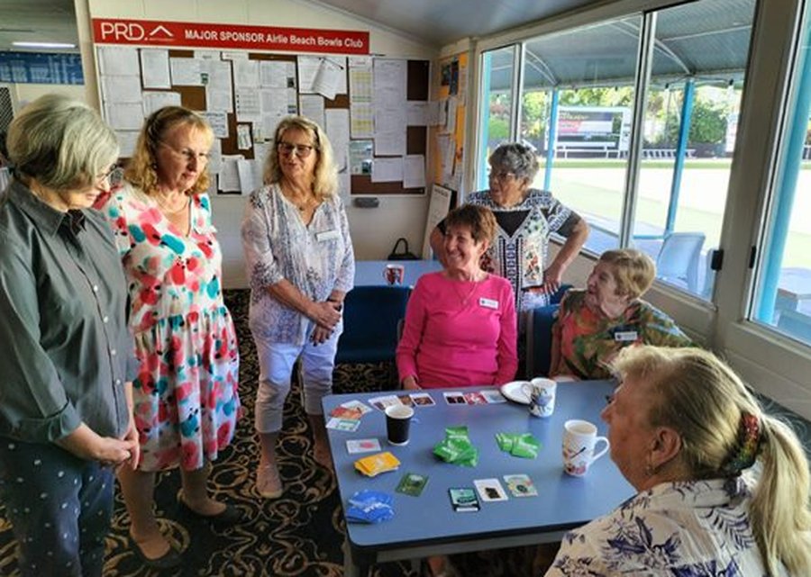 A group of older players around a table at a bowls club, playing Carked It cards together