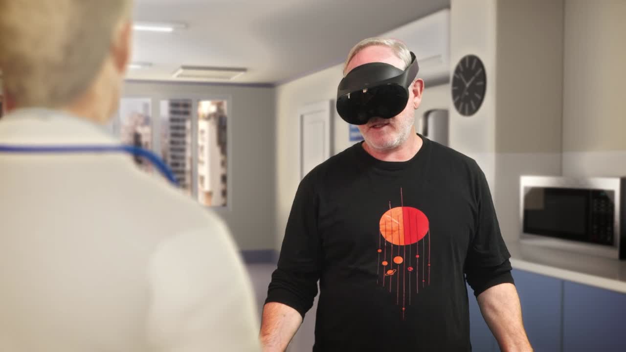 A man wearing a headset stands in a home kitchen, a second person in the foreground, a microwave and clock on the wall behind him. A VR scenario set in a domestic kitchen.