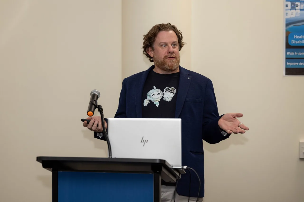 Simon Lowe speaks from a lectern at the PTR VR Library launch in Townsville, a frame from the recording of the evening.