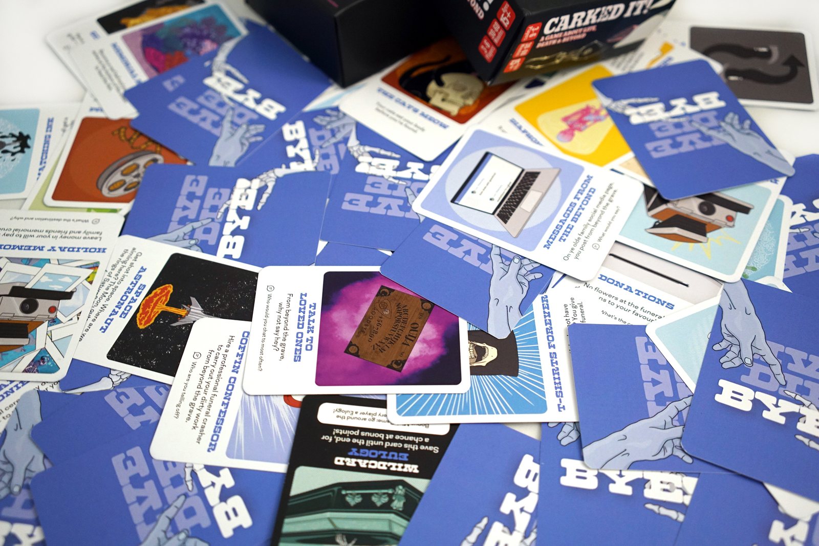 Blue cards from the BYE deck scattered face up, with titles about messages from the beyond, talking to loved ones, coffin confessions and donations.