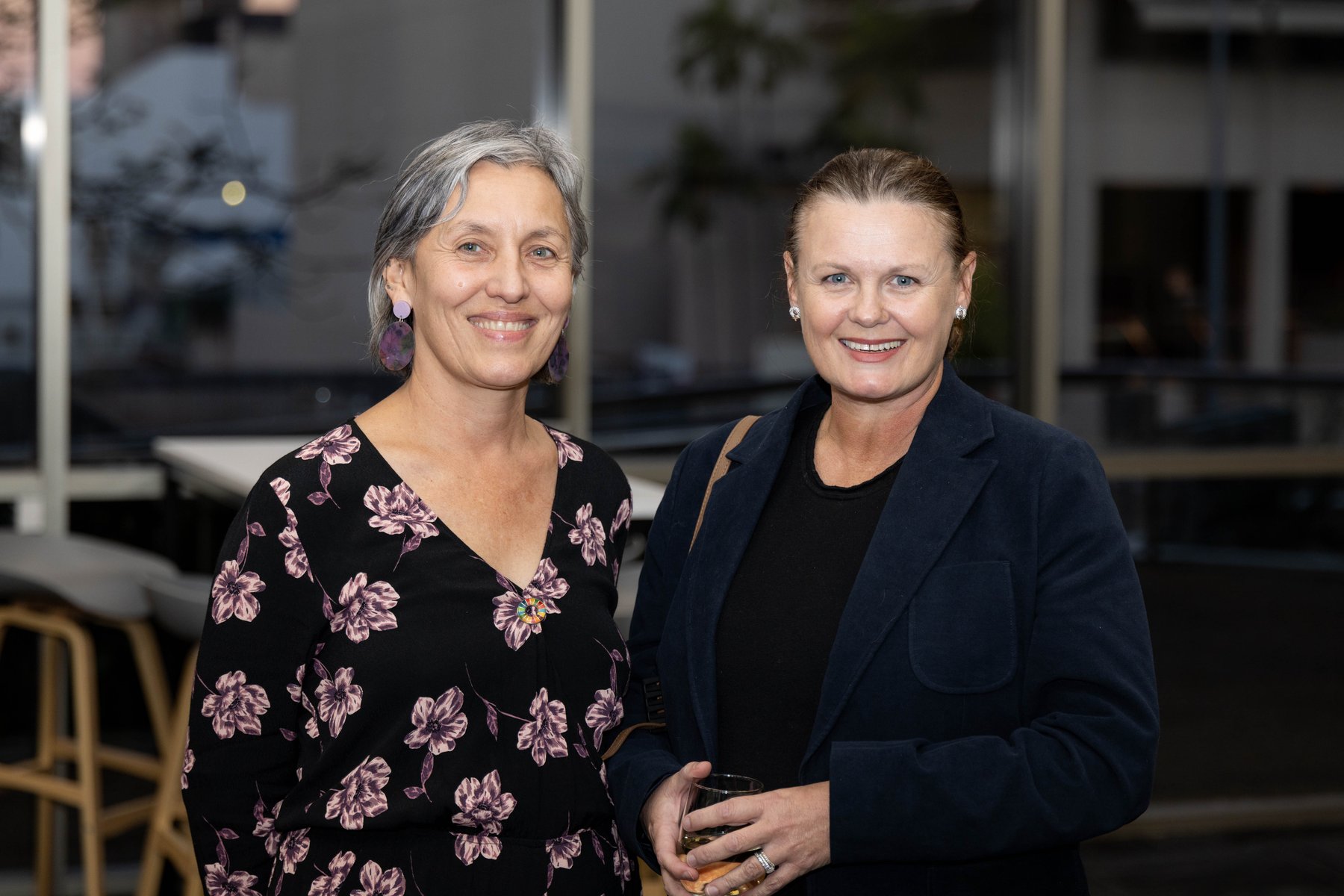 Two smiling women, one with short silver hair in a floral dress, standing together at a PTR community event