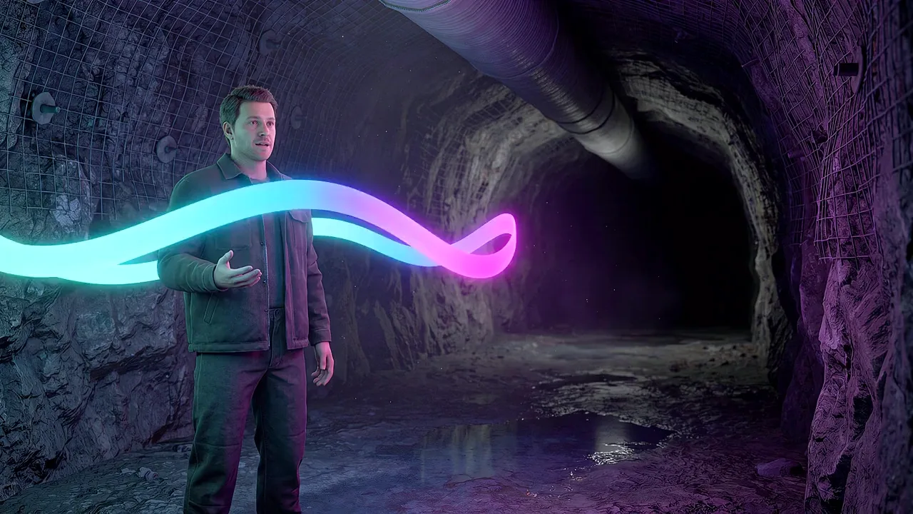 A man stands in a rock tunnel, a ribbon of light curving through the drift as he speaks.