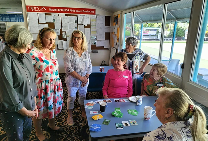 A group of older players around a table at a bowls club, playing the Carked It! card game.