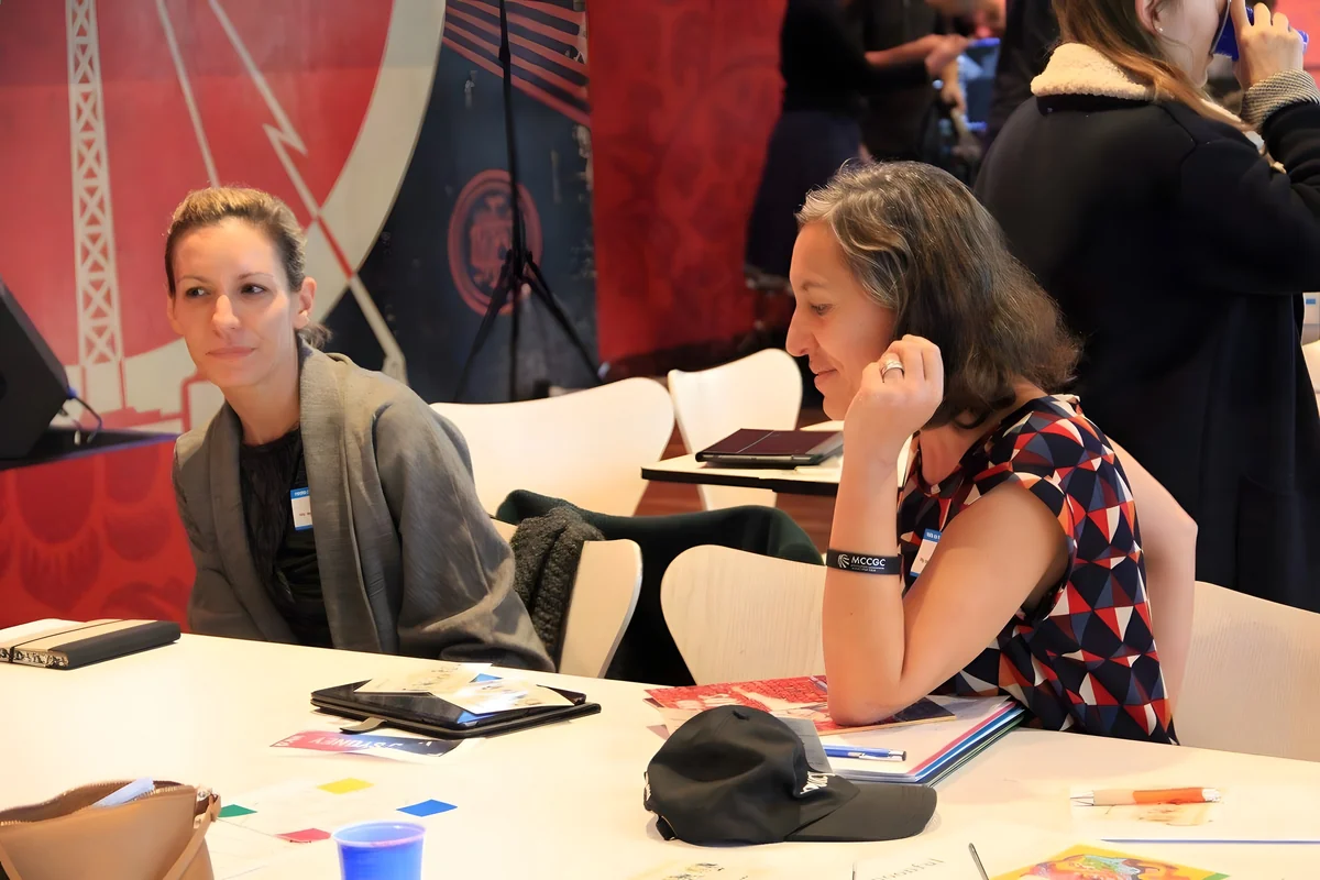 Two participants at a workshop table covered in printed cards and tablets, mid-discussion.