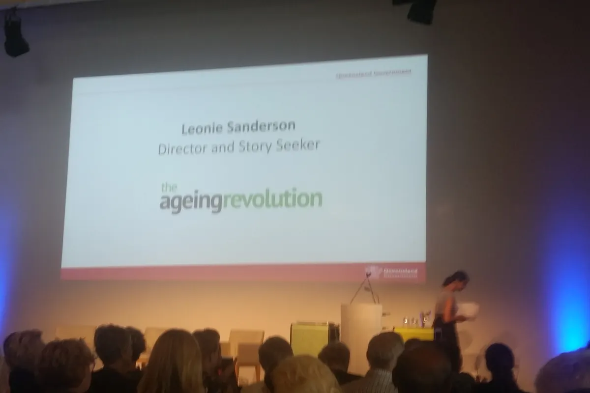 An audience faces a large screen whose slide reads Leonie Sanderson, Director and Story Seeker, with The Ageing Revolution's logo.